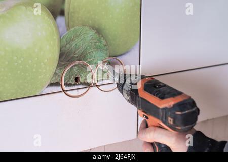 Ein Mann mit einem Metallschneider schneidet ein Loch in eine Kachel für eine Steckdose. Renovierung und Verbesserung des Hauses. Stockfoto