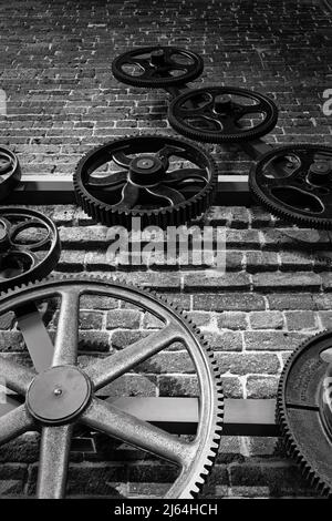 Große Zahnräder aus alten Textilmühlen, die in einem künstlerischen Muster auf einer Ziegelwand des Lowell Historic Park Visitors Center verteilt sind. Lowell, Massachusetts. V Stockfoto