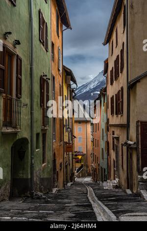 Briancon, Frankreich - 15 Mär 2022: Bunte mittelalterliche Straße von Briancon mit Blick auf die verschneiten Berge; schönste Straßen der Welt Tapete Stockfoto