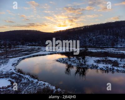 Winter Luftaufnahme auf verschneiten Flusskurve mit szenischer Reflexion. Region Smijewski auf dem Fluss Siwerskyi Donez in der Ukraine. Sonnenuntergangssonne in Wolken über dem Hügel Stockfoto