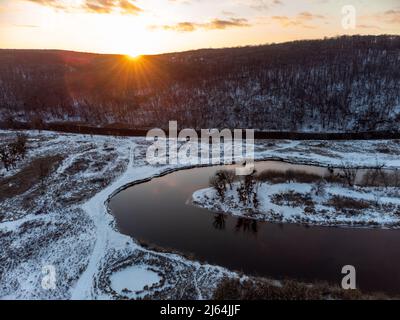 Winter Luftaufnahme auf verschneiten Fluss Kurve. Region Smijewski auf dem Fluss Siwerskyi Donez in der Ukraine. Die Sonnenuntergangssonne scheint über einem bewaldeten Hügel Stockfoto