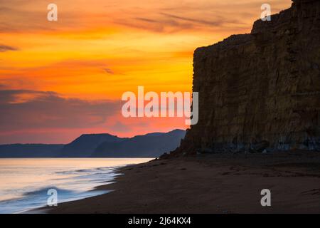 Burton Bradstock, Dorset, Großbritannien. 27.. April 2022. Wetter in Großbritannien. Der Himmel leuchtet orange über dem Strand und den Klippen bei Sonnenuntergang am Burton Bradstock in Dorset und am Ende eines Tages voller Sonneneinflüsse. Bildnachweis: Graham Hunt/Alamy Live News Stockfoto