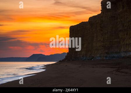 Burton Bradstock, Dorset, Großbritannien. 27.. April 2022. Wetter in Großbritannien. Der Himmel leuchtet orange über dem Strand und den Klippen bei Sonnenuntergang am Burton Bradstock in Dorset und am Ende eines Tages voller Sonneneinflüsse. Bildnachweis: Graham Hunt/Alamy Live News Stockfoto