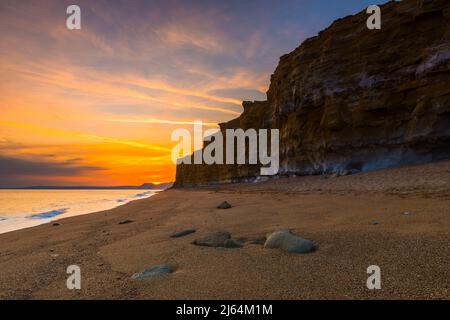 Burton Bradstock, Dorset, Großbritannien. 27.. April 2022. Wetter in Großbritannien. Der Himmel leuchtet orange über dem Strand und den Klippen bei Sonnenuntergang am Burton Bradstock in Dorset und am Ende eines Tages voller Sonneneinflüsse. Bildnachweis: Graham Hunt/Alamy Live News Stockfoto