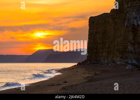 Burton Bradstock, Dorset, Großbritannien. 27.. April 2022. Wetter in Großbritannien. Der Himmel leuchtet orange über dem Strand und den Klippen bei Sonnenuntergang am Burton Bradstock in Dorset und am Ende eines Tages voller Sonneneinflüsse. Bildnachweis: Graham Hunt/Alamy Live News Stockfoto