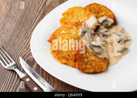 Pfannkuchen mit gebratenen Pilzen und Zwiebeln. Kartoffelpfannkuchen mit Pilzen und Sauerrahm. Ukrainische Küche, europäische Küche. Stockfoto