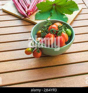 Frisch gepflückte italienische Grappoli d’Inverno Wintertrauben-Tomaten und Jing Orangen-Okra-Schoten auf einem Tisch im Freien mit Platz für Kopien Stockfoto