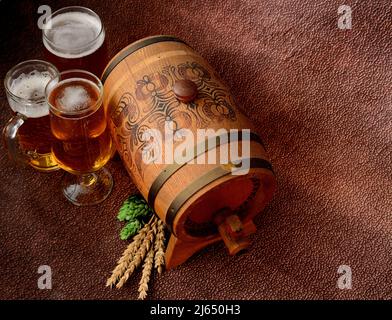 Drei verschiedene Gläser mit hellem Bier, einem Holzfass, Ähren aus Malz und Hopfen auf braunem abstraktem Hintergrund. Draufsicht, flach liegend. Stockfoto