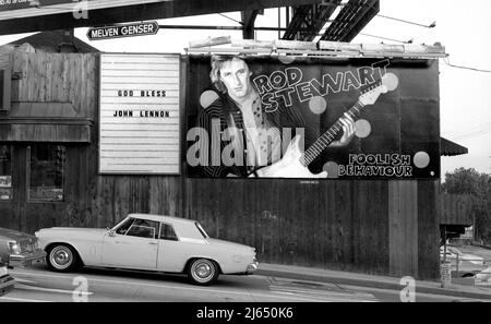 Schild zum Gedenken an den Tod von John Lennon im Jahr 1980 neben einer Plakatwand für Rod Stewart an der Seite des Licorice Pizza Plattenladens am Sunset Strip. Stockfoto