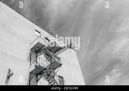 NEW ORLEANS, LA, USA - 19. APRIL 2022: Schwarz-Weiß-Bild einer Feuerflucht auf der Seite eines hohen Gebäudes und wispige Wolken im Hintergrund Stockfoto