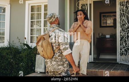 Patriotischer junger Soldat überraschte seine Frau mit seiner Heimkehr. Mutiger junger Militärangehöriger, der sich mit seiner Frau wiedervereinigt, nachdem er seinem Land in der Dienst gestellt hatte Stockfoto