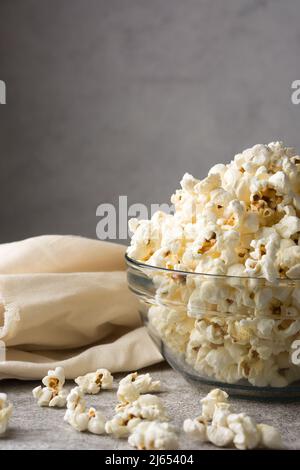 Popcorn in einer Glastasse, köstlicher, fettarmer, gesunder Snack in einem Behälter mit verstreuter Oberfläche, auf einer texturierten Tischplatte, Platz zum Kopieren Stockfoto
