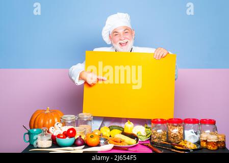 Chefkoch zeigt sich an einem leeren Brett. Cook zeigte ein leeres Brett. Der Koch zeigt mit dem Finger auf das leere Brettmenü. Stockfoto