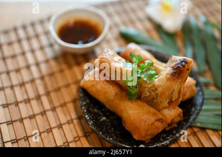 Leckeres asiatisches Gemüse Frühlingsrollen auf einem minimalen schwarzen Teller serviert mit spezieller süßer, würziger Sauce. Stockfoto