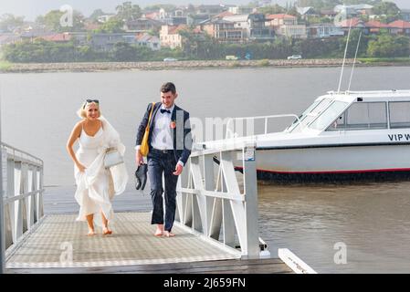 Das gerade verheiratete Paar Amy und Kieran machen sich barfuß und im Regen auf eine Bootsrampe, von einer Wassertaxi-Fahrt im Hafen von Sydney bis zu ihrer Rezeption Stockfoto