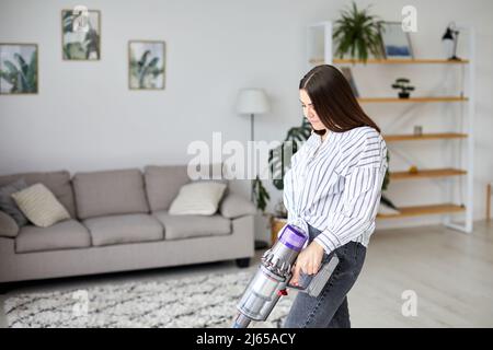 Frau, die den Boden mit einem kabellosen Handstaubsauger im Wohnzimmer zu Hause reinigt. Hausfrau bei der Hausarbeit Stockfoto