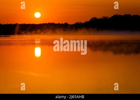 Hannover, Deutschland. 28. April 2022. Die Sonne geht über dem Altwarmbüchensee auf, während Bodennebel über die Wasseroberfläche driftet. Quelle: Moritz Frankenberg/dpa/Alamy Live News Stockfoto