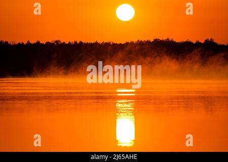 Hannover, Deutschland. 28. April 2022. Die Sonne geht über dem Altwarmbüchensee auf, während Bodennebel über die Wasseroberfläche driftet. Quelle: Moritz Frankenberg/dpa/Alamy Live News Stockfoto