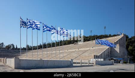 Athen, Griechenland. Das Panathenaic Stadium oder Kallimarmarmaro. Alte Marmor-Sportarena. Griechische Flaggen auf Fahnenmasten winken an einem sonnigen Tag, blauer Himmel ruckartig Stockfoto