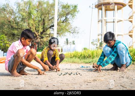 Indische Dorfkinder spielen goli oder Murmeln in der Nähe des Reisfeldes - Konzept für traditionelles Spiel, Sommerferien und Freizeitaktivitäten. Stockfoto