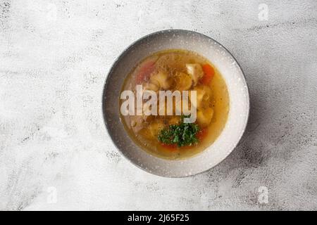Leckere Hühnersuppe-Bouillon mit Knödeln, Hühnerfleisch und Petersilie in einer weißen Schüssel. Isoliert auf Marmorboden. Gesunde Speisekarte Stockfoto