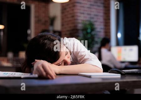 Müde Büroangestellte mit Burnout-Syndrom schlafen bei der Arbeit wegen extremer Müdigkeit. Erschöpfter Manager, der nach Überstunden an Müdigkeit leidet. Stockfoto