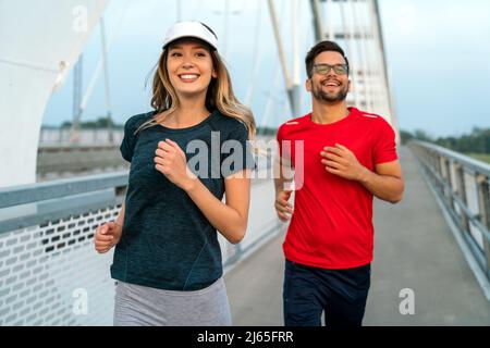 Workout am frühen Morgen. Glückliches Paar, das über die Brücke läuft. Ein gesunder Lebensstil. Stockfoto