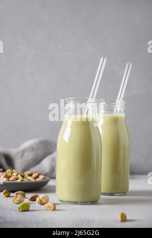 Pistazien-Milch in Flaschen auf grauem Hintergrund. Horizontale Ausrichtung. Laktosefrei. Vegane nussige Milch auf pflanzlicher Basis. Vertikal. Stockfoto