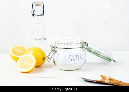 Backpulver im Glas, Essig, Zitrone, Holzlöffel auf weißem Hintergrund. Das Konzept, Flecken auf der Kleidung zu entfernen. Hochwertige Fotos Stockfoto
