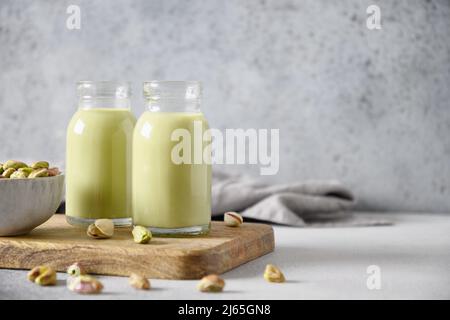 Pistazien-Milch in Flaschen auf grauem Hintergrund. Horizontale Ausrichtung. Laktosefrei. Vegane nussige Milch auf pflanzlicher Basis. Speicherplatz kopieren. Stockfoto