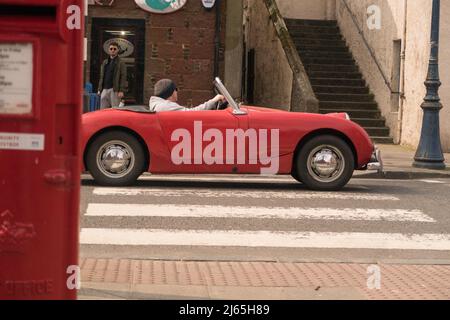 Ein rotes Cabrio-Auto von Austin Healey Sprite, das durch ein Dorf in Schottland fährt. Stockfoto