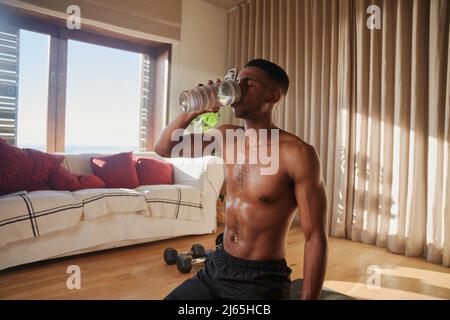 Afroamerikanischer junger schwarzer Mann, der nach dem Training zu Hause in seinem Wohnzimmer Trinkwasser ausübt Stockfoto