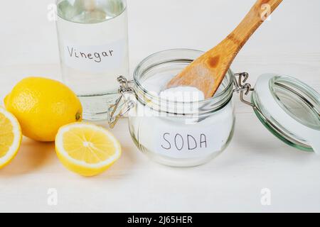 Backpulver im Glas, Essig, Zitrone, Holzlöffel auf weißem Hintergrund. Das Konzept, Flecken auf der Kleidung zu entfernen. Hochwertige Fotos Stockfoto