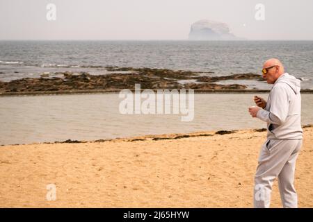 Ein Mann, der am Strand in North Berwick ein Eis isst, mit dem Bass Rock im Hintergrund Stockfoto