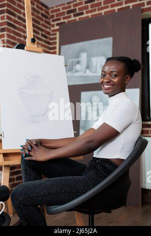 Porträt eines afroamerikanischen Studenten, der Kunstunterricht attesting, der im Kreativitätsstudio eine Ziehstunde genießt. Malerin Frau Zeichnung Vase Modell auf weißer Leinwand arbeiten an der grafischen Technik. Kreatives Konzept Stockfoto