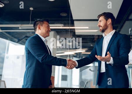 Zwei reife, vielfältige Geschäftspartner schütteln sich nach erfolgreichem Abschluss im modernen Büro Stockfoto