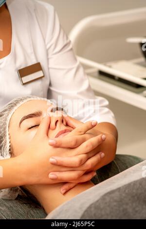 Schöne junge kaukasische Frau mit geschlossenen Augen erhält eine Gesichtsmassage in einem Schönheitssalon Stockfoto