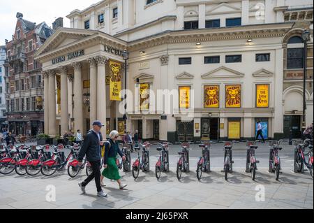 Ältere Männer und Frauen laufen am Lyceum Theatre in der Wellington Street an einer Reihe von Mietfahrrädern von Santander vorbei, die gegenüber liegen. London, England, Großbritannien Stockfoto