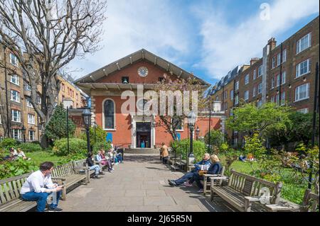 An einem sonnigen Frühlingstag saßen Menschen auf Bänken, um sich im Garten der St. Paul’s Church in Covent Garden zu unterhalten und zu entspannen. London, England, Großbritannien. Stockfoto