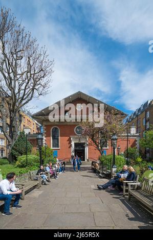 An einem sonnigen Frühlingstag saßen Menschen auf Bänken, um sich im Garten der St. Paul’s Church in Covent Garden zu unterhalten und zu entspannen. London, England, Großbritannien. Stockfoto