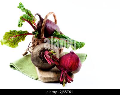 Frische Bio-Rübenwurzeln mit grünen Rübenoberteile und einer Hälfte in Weidenkorb auf Holzbrett und Serviette isoliert auf weißem Hintergrund Stockfoto