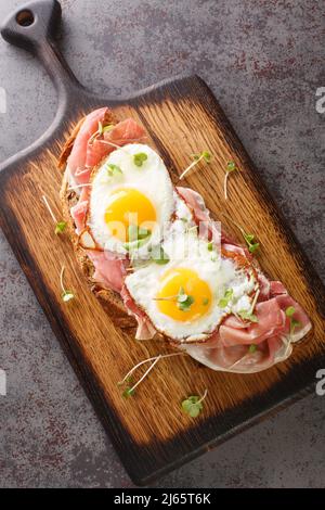 Strammer Max German Sandwich mit geräuchertem Schinken und Eiern auf dem Holzbrett auf dem Tisch. Vertikale Draufsicht von oben Stockfoto
