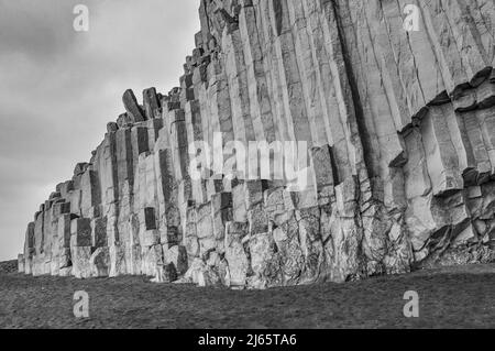 Schwarzweißaufnahme der Basaltsäulen am Reynisfjara-Strand, rechts die Höhle Reynishellir (Südland) - Schwarz-Weiß-Aufnahme von Basaltsäulen in Island Stockfoto