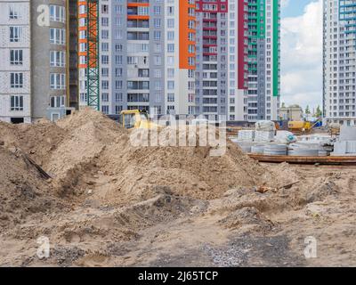 Eine Baustelle mit Sandhaufen, Betonringen im Vordergrund und neuen bunten Hochhäusern und Baugeräten im Hintergrund Stockfoto