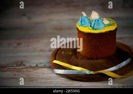 Osterkarte. Osterkuchen mit Creme in den Farben der ukrainischen Flagge auf einem Holzbrett dekoriert Stockfoto