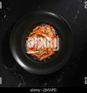 Funchoza mit Huhn und Gemüse auf schwarzem Hintergrund, Platz kopieren. Glasnudeln, traditionelle asiatische Speisen, Braten Sie Nudeln oder Wok-Nudeln in einem BL Stockfoto