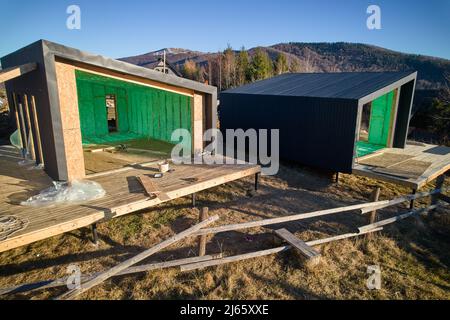 Luftaufnahme von zwei Holzrahmenhäusern im skandinavischen Stil, die mit Polyurethanschaum isoliert sind. Bau- und Isolierkonzept. Stockfoto