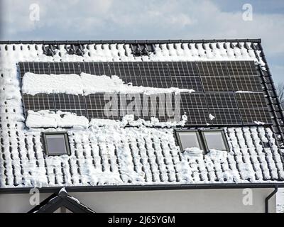 Nahaufnahme von Solarpaneelen, die auf dem mit Schnee bedeckten Familienhausdach montiert sind Stockfoto