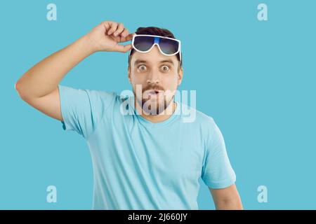 Der Mann hebt seine Sonnenbrille und sieht etwas mit einem witzig überraschten, fröhlichen Gesichtsausdruck an Stockfoto