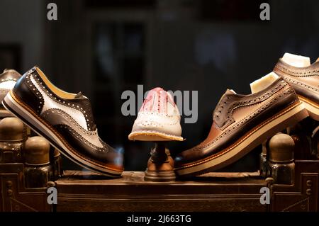 Brogue-Schuhe mit Gummisohlen stehen nachts in einer Schaufensterauslage einer Schuhmacherwerkstatt. Sie stehen auf einer Vintage-Schuhpflegebox. Stockfoto